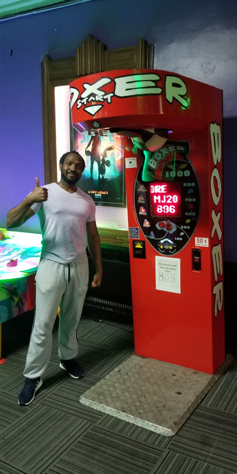 High score holder giving a thumbs up beside the Boxer arcade machine